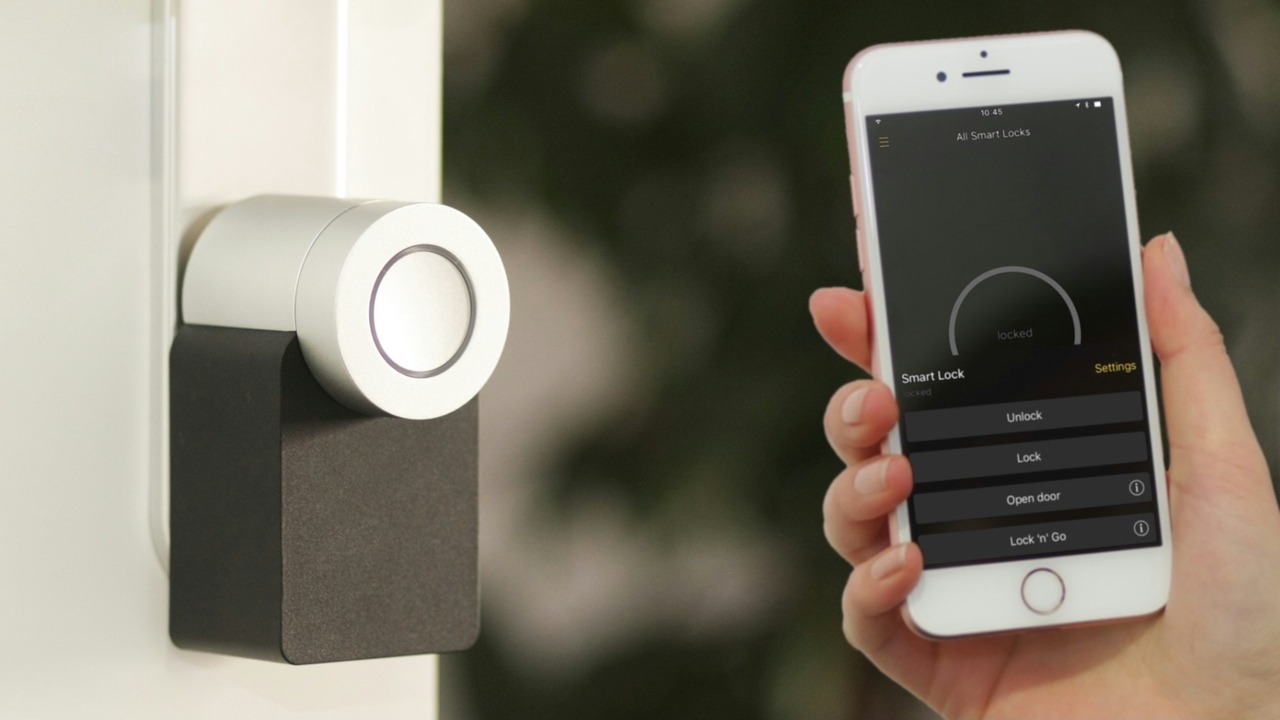 A modern smart lock mounted on a white door, featuring a sleek design with a circular touch interface, alongside a hand holding a smartphone displaying the smart lock app with options to lock, unlock, and open the door.